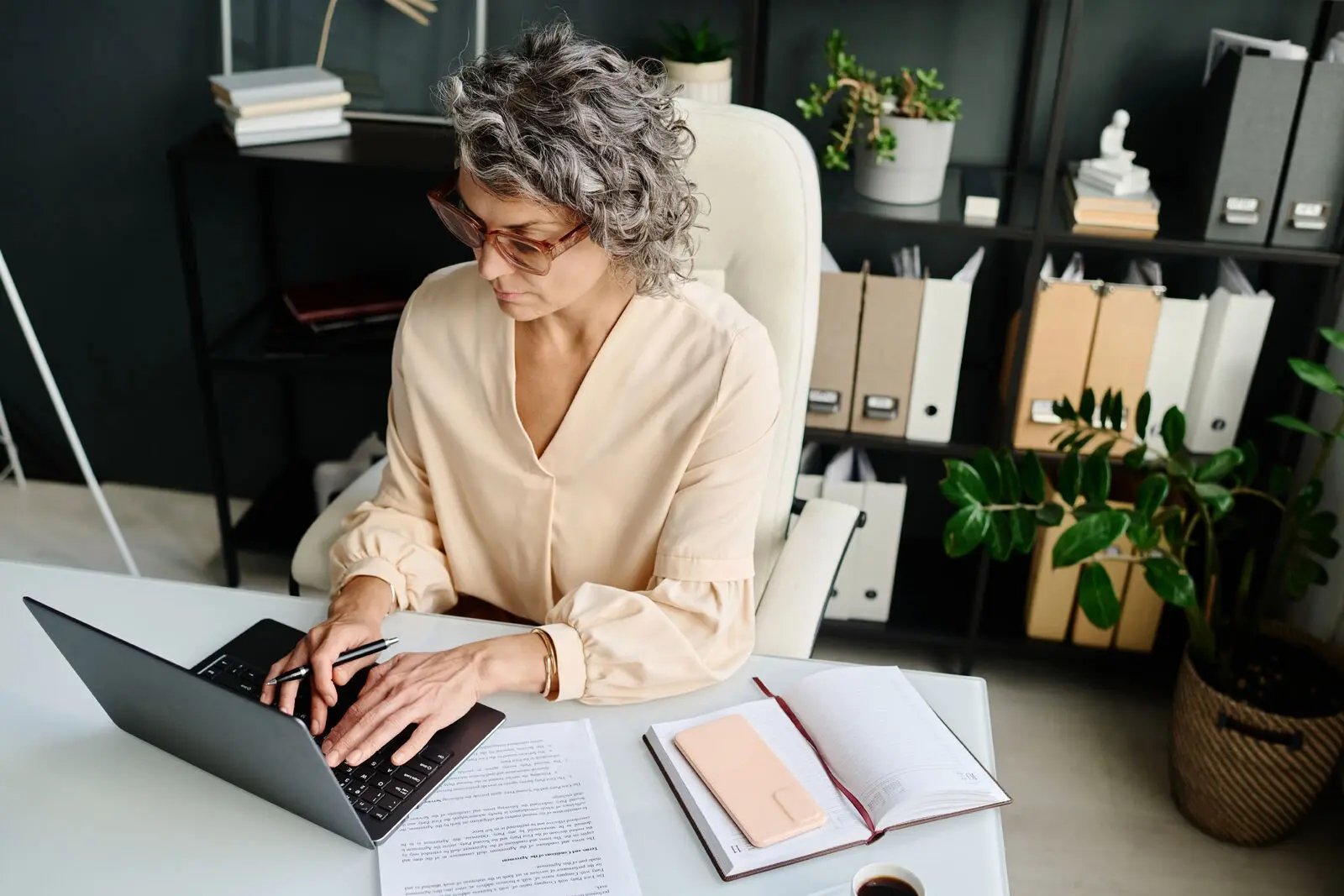 Older female professional, sat at the desk working on her laptop